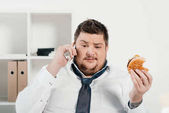 nadváhou podnikatel rozhovor na smartphone a zároveň jíst hamburger v úřadu