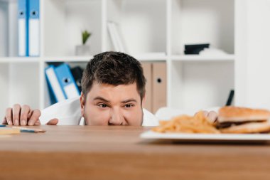 hamburger ve patates kızartması işyerinde bakarak kilolu iş adamı