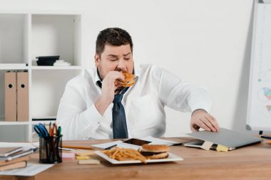 Hamburger yeme ve dizüstü bilgisayar kullanma office kilolu işadamı