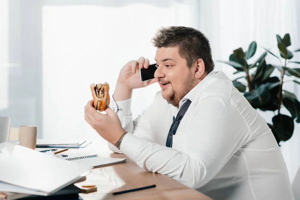 Överviktig Affärsman Talar Smartphone Medan Man Äter Hamburgare Office — Stockfoto