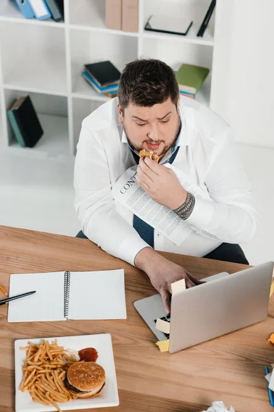 Övervikt Affärsman Äta Skräpmat Medan Arbetar Med Laptop Office — Gratis stockfoto