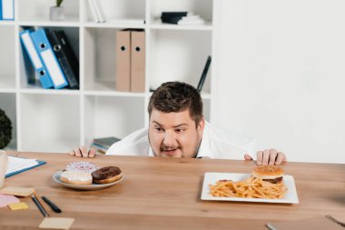 şişman işadamı çörek veya hamburger patates kızartması ile öğle yemeği için seçme