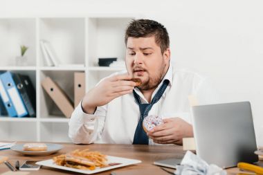 kilolu işadamı işyerinde çörek, hamburger ve kızarmış patates yeme