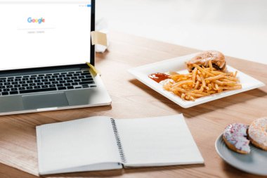google web sitesi, not defteri, çörek ve patates kızartması işyerinde hamburger ile dizüstü bilgisayar 