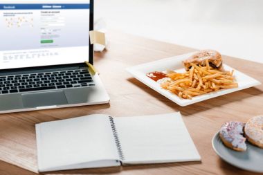 Web sitesi facebook, not defteri, çörek ve patates kızartması işyerinde hamburger ile dizüstü bilgisayar 