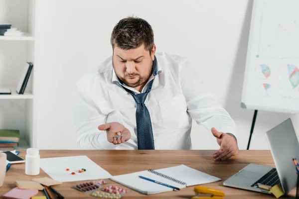 Übergewichtiger Geschäftsmann Sitzt Arbeitsplatz Und Schaut Sich Pillen — Stockfoto