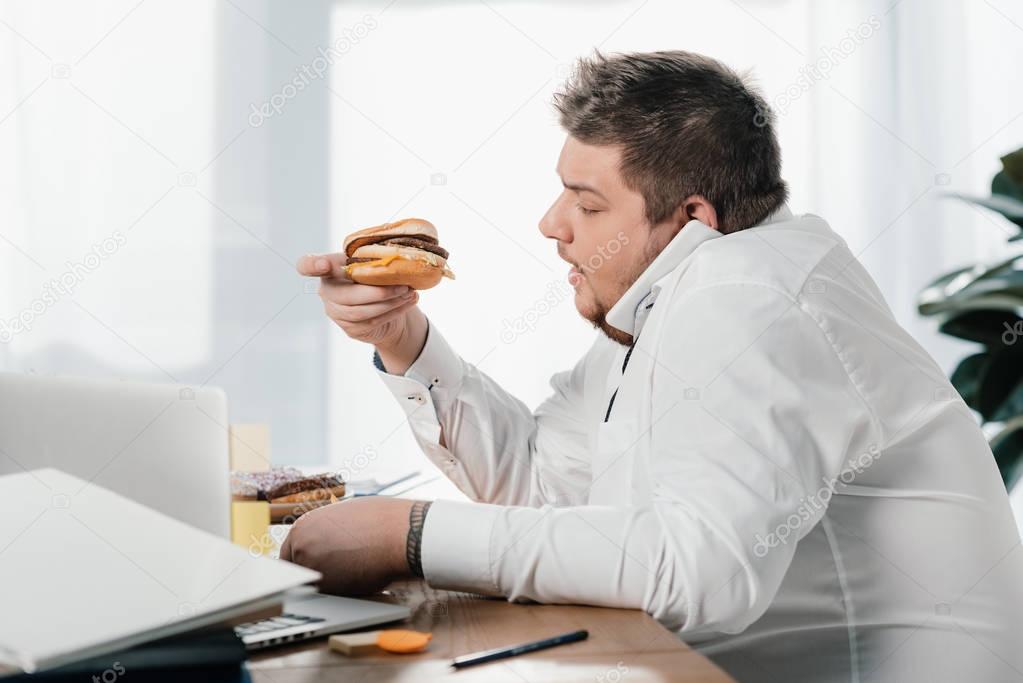 overweight businessman eating hamburger while working in office