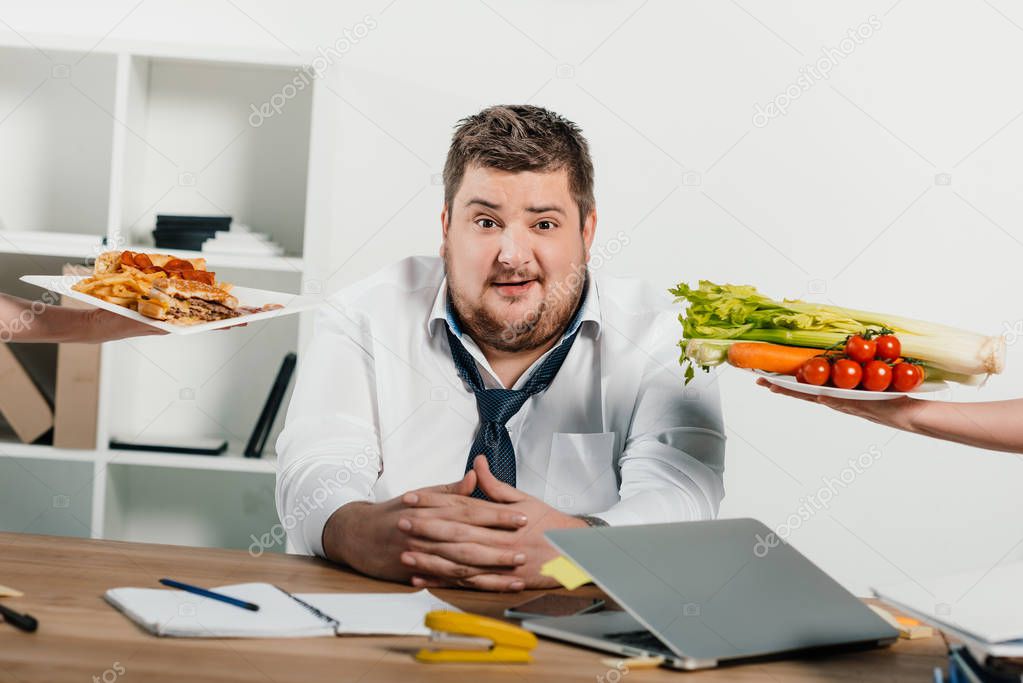 overweight businessman choosing healthy or junk food at workplace in office