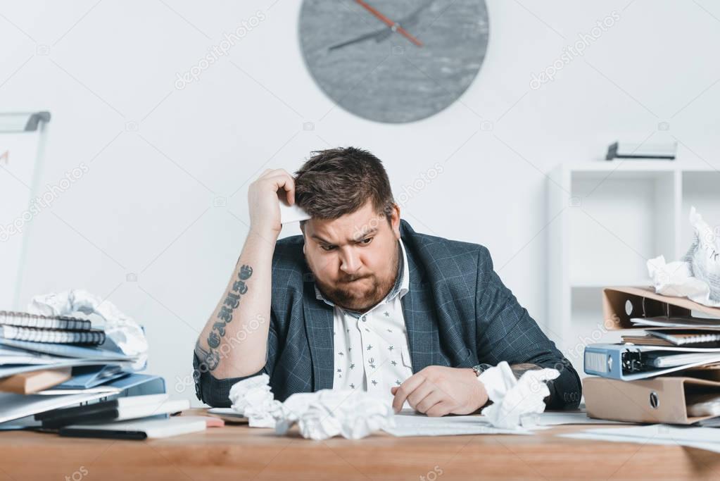 confused overweight businessman in suit working with documents in office