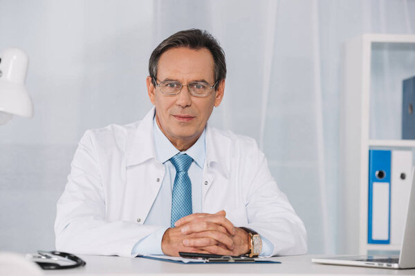 handsome doctor sitting at working table and looking at camera