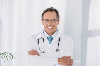 çapraz elleriyle ayakta ve kameraya bakarak doktor gülümseyen