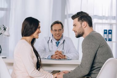 happy couple holding hands at clinic and looking at each other clipart