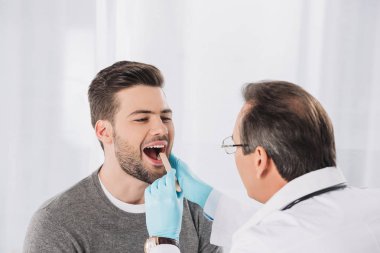 doctor examining patient throat in medical gloves clipart