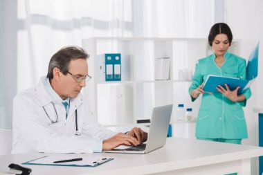 nurse searching something in folder and doctor using laptop