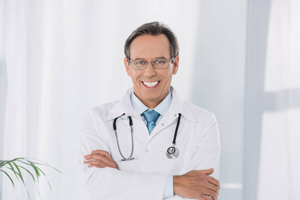 smiling doctor standing with crossed hands and looking at camera