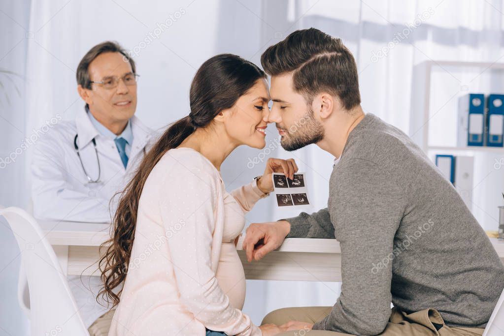 happy couple holding photo of ultrasound diagnostics and kissing