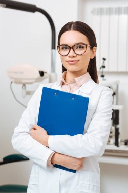 Beyaz önlük içinde gülümseyen optometrist kamera Kliniği bakarak elinde Not Defteri ile portresi