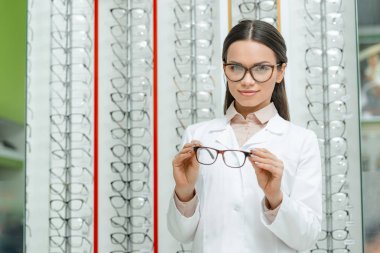 Optik Gözlük çifti holding beyaz paltolu gülümseyen gözlükçü portresi