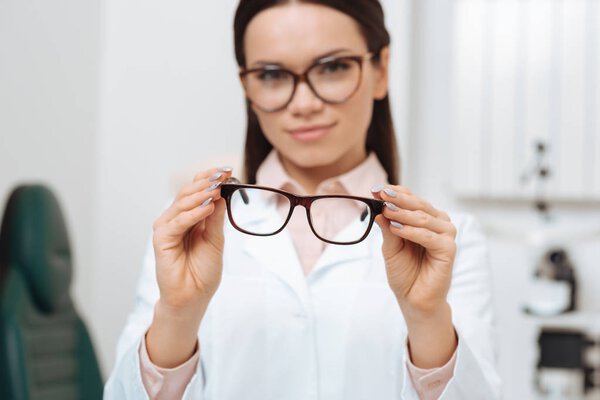 selective focus of ophthalmologist holding pair of eyeglasses in hands in clinic