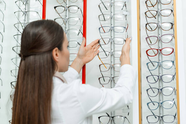 selective focus of optometrist taking eyeglasses from shelf in optics