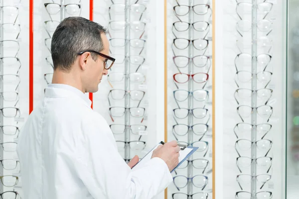 Side View Optometrist Making Notes While Standing Shelves Eyeglasses Optics — Free Stock Photo