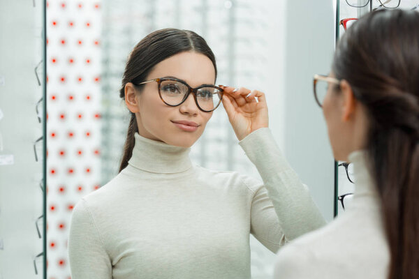 portrait of young smiling girl choosing pair of eyeglasses in optics