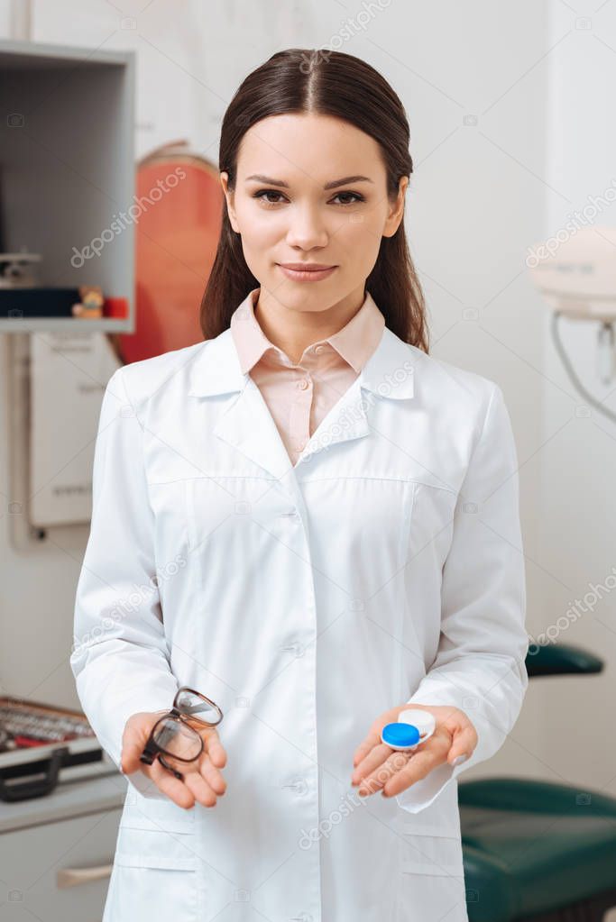 portrait of optometrist in white coat holding eyeglasses and contact lens in clinic
