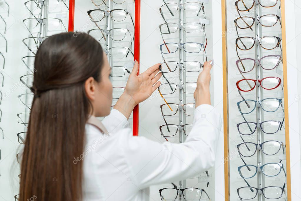 selective focus of optometrist taking eyeglasses from shelf in optics