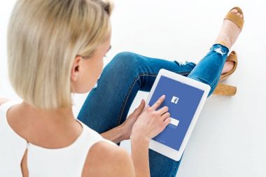 Sarışın kadın ile facebook app, üzerinde beyaz izole dijital tablet kullanarak arkadan görünüm