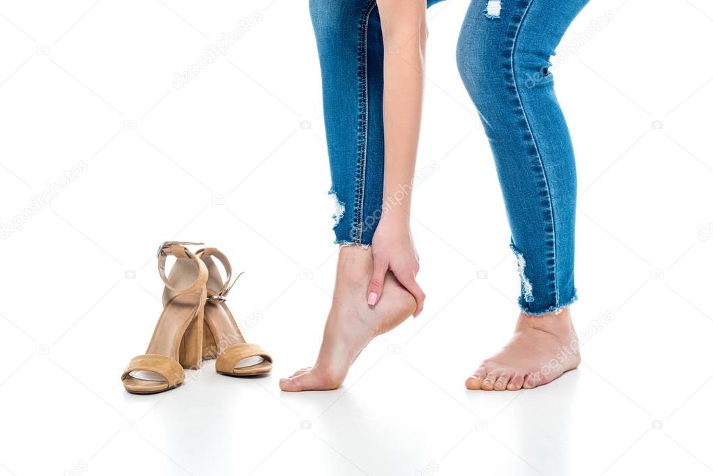 cropped view of tired barefoot woman standing near heels, isolated on white
