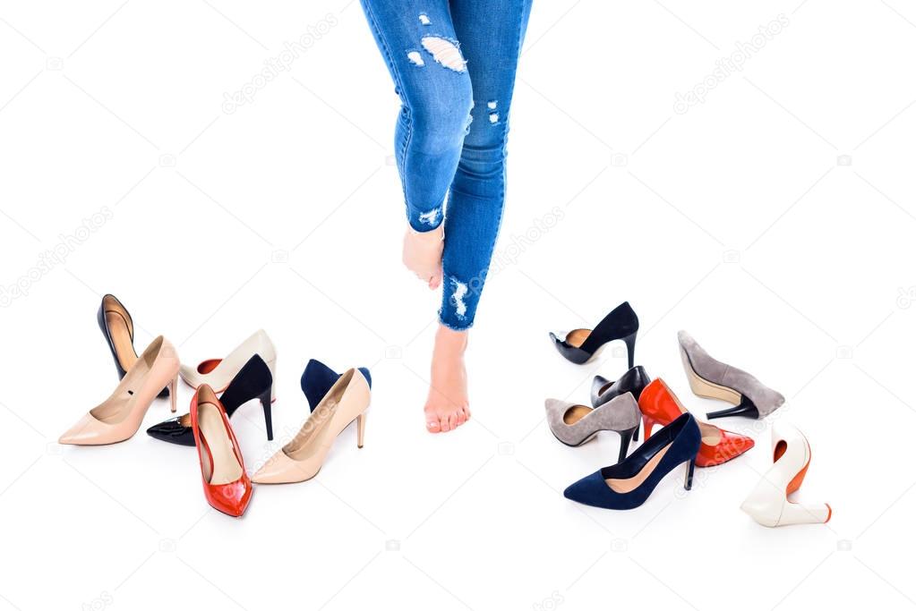 cropped view of barefoot girl standing near heels, isolated on white