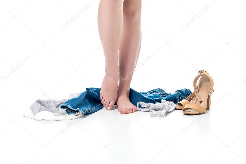cropped view of female legs standing with clothes around, isolated on white