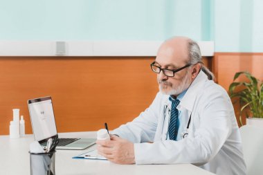Not defteri Kliniği içinde laptop ile işyerinde notlar yapma odaklı kıdemli doktor yan görünüm
