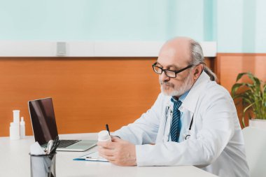 Not defteri Kliniği içinde laptop ile işyerinde notlar yapma odaklı kıdemli doktor yan görünüm