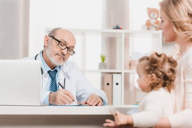Kıdemli doktor anne ve küçük kızı Kliniği tarafından masada oturan sırasında Notlar
