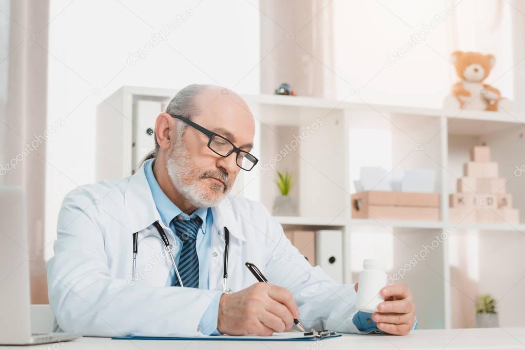 portrait of focused senior doctor making notes on notepad at workplace in clinic