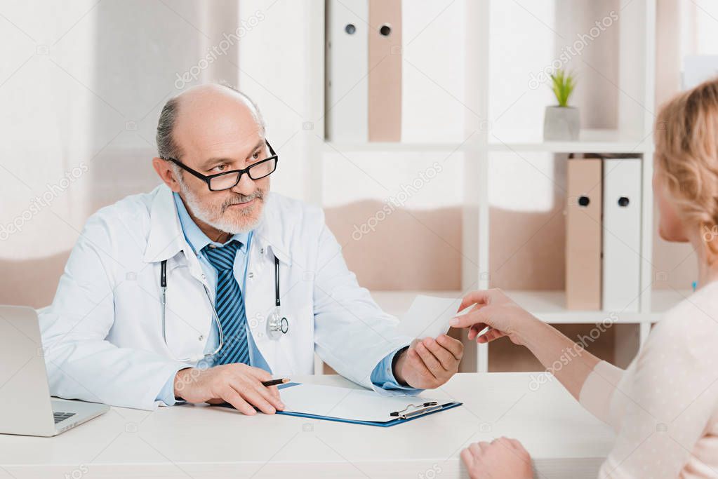 partial view of senior doctor giving prescription to patient at workplace in clinic