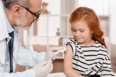 doctor in medical gloves making injection to little girl in clinic clipart