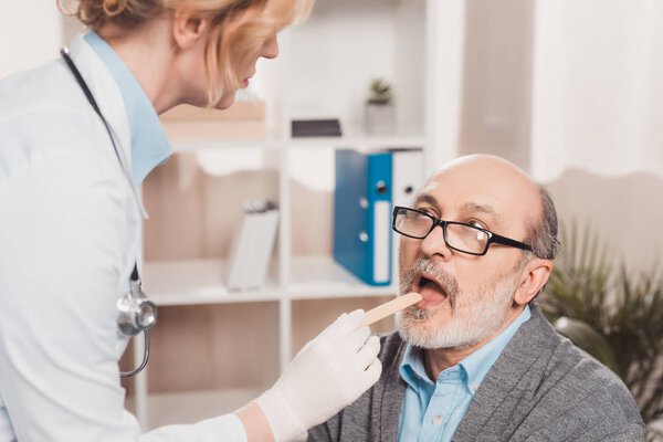 selective focus of doctor in medical gloves checking patients throat in clinic