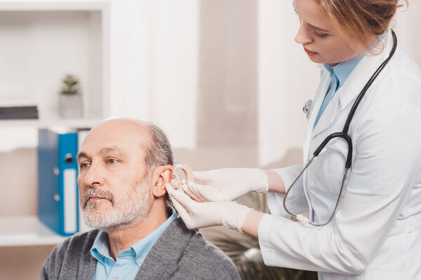 female doctor in medical gloves examining senior patient in clinic