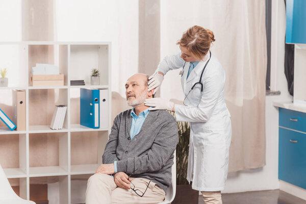 female doctor in medical gloves examining senior patient in clinic