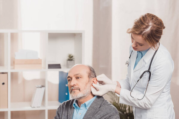 female doctor in medical gloves examining senior patient in clinic