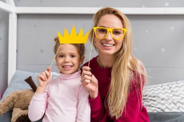 Anne ve kızı oyuncak maskeli balo crown ve gözlük ile gülümseyen