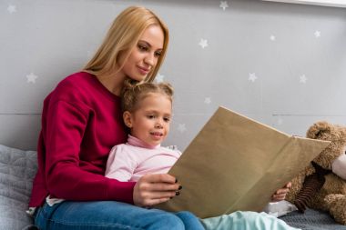 genç anne ve kızı yatağa oturmuş ve birlikte kitap okuma