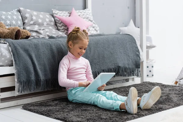 katta oturan ve tablet kullanarak gülümseyen küçük çocuk