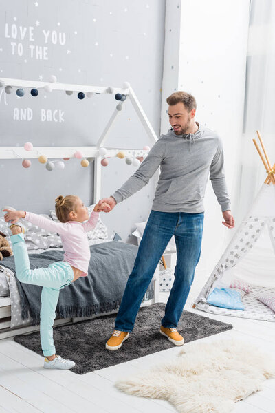 handsome young father dancing with daughter in kid bedroom