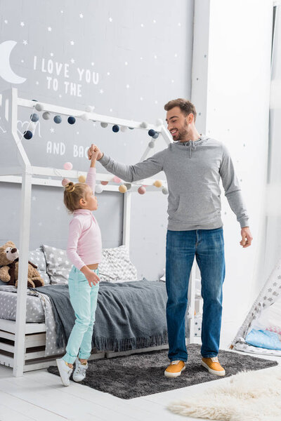 happy young father dancing with daughter in kid bedroom