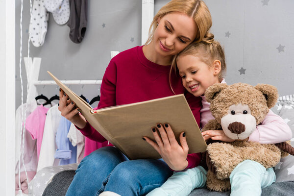 mother and daughter sitting on bed and reading book together