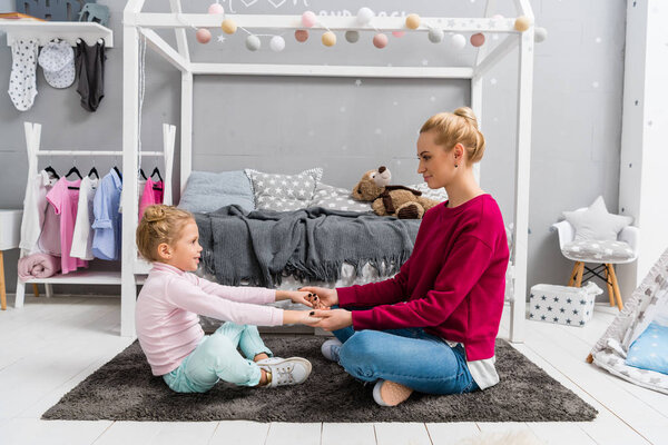 mother and daughter sitting on floor on kid bedroom and holding hands