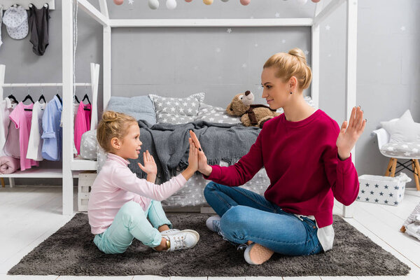 mother and daughter playing pattycake while sitting on floor